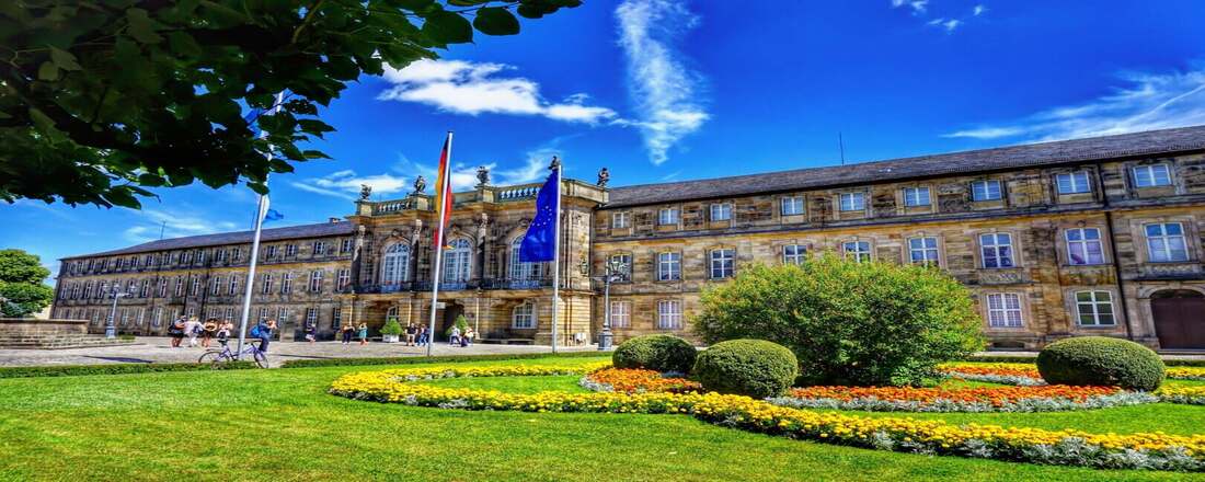 historic palace with ornate architecture surrounded by flower gardens and flags