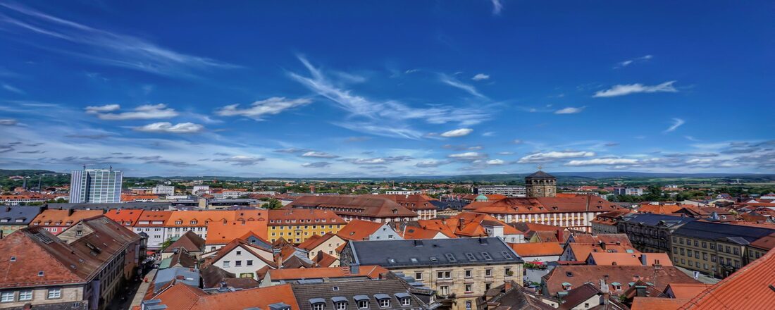 A panoramic view of Bayreuth with red tiled roofs, historic buildings and a green landscape under a blue sky